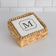 a square cake with the letter m on it in a wicker basket next to a white tile wall