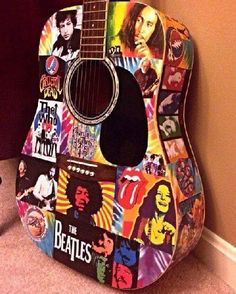 a guitar covered in stickers sitting on the floor next to a wall with a carpet