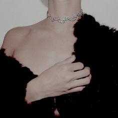 a woman wearing a black fur coat and diamond choker with her hands on her chest