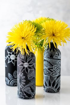 three black and white vases with yellow flowers in them