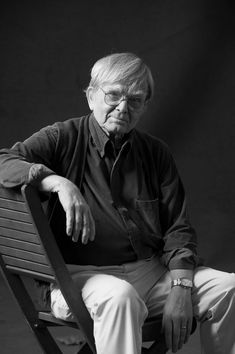 black and white photograph of an older man sitting on a bench with his hands folded