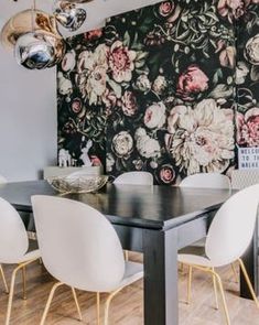 a dining room table with white chairs and a black floral wallpaper behind the table