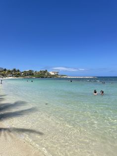 people are swimming in the clear blue water on a sunny day at an ocean beach