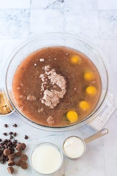 ingredients to make chocolate cake in a mixing bowl on a marble counter top with milk, eggs and chocolate chips