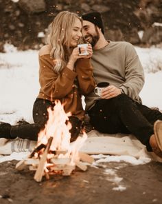 a man and woman sitting next to a campfire drinking coffee