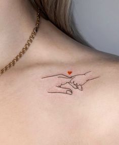 a woman's chest with two hands holding a heart tattoo on her left side