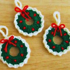 three crocheted christmas ornaments with red bows on them sitting on a wooden surface