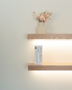 two wooden shelves with books and flowers on them in front of a wall mounted light