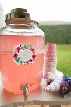 a pink beverage dispenser sitting on top of a table next to flowers