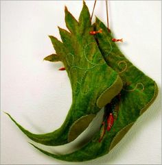 two green leaves hanging from hooks on a white wall with red string attached to them