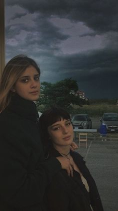 two young women standing next to each other in front of a parking lot at night