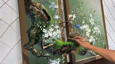 a person is painting flowers and birds on a canvas