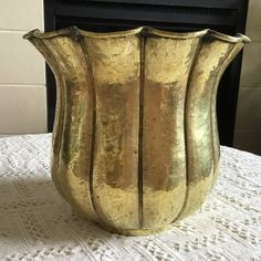 a gold colored vase sitting on top of a white tablecloth next to a fireplace