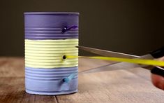 a person is cutting paper with scissors on a wooden table next to a tin can