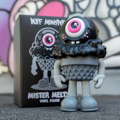 a small toy is standing next to a box with graffiti on the wall behind it