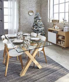 a dining room table with white chairs and a christmas tree on the wall behind it