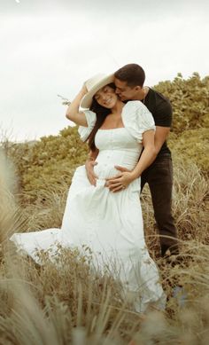 a man and woman are standing in tall grass with their arms around each other as they hug