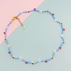 a blue beaded necklace with white and yellow flowers on it, next to a pink background