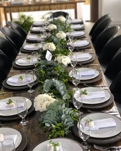 the table is set with white and green flowers, greenery, and silverware