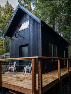 a small cabin in the woods with deck and chairs