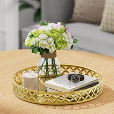 a gold tray with flowers and books on it sitting on a table in front of a couch