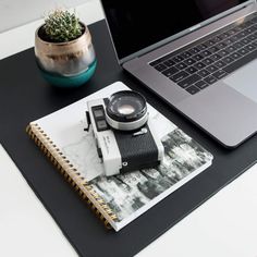 an open laptop computer sitting on top of a desk next to a camera and notebook