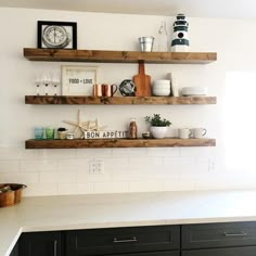 three wooden shelves with various items on them in a kitchen, one has a clock and the other is empty