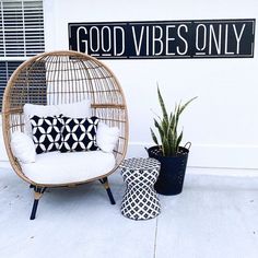 a wicker chair with black and white pillows sits in front of a sign that says good vibes only