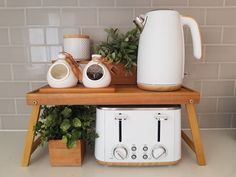 a white toaster sitting on top of a wooden table next to a potted plant