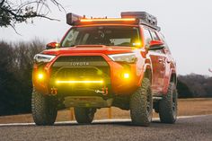 an orange toyota truck with its lights on driving down the road in front of some trees