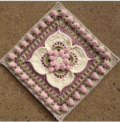 a crocheted square with a flower on it sitting on the ground in front of a wall