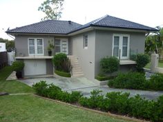 a grey house with white shutters and bushes