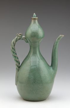 a green ceramic teapot with a twisted handle