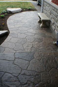 a person sitting on a bench in front of a brick wall and grass area next to a sidewalk