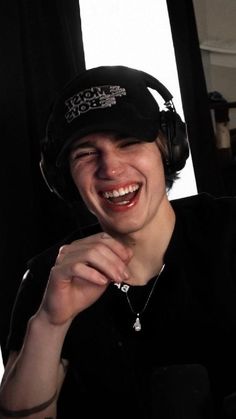 a young man wearing headphones and smiling at the camera while sitting in front of a window