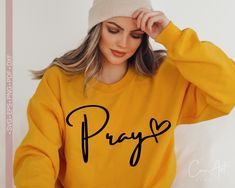 a woman wearing a yellow sweatshirt with the word pray printed on it and a beanie