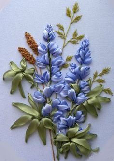 a close up of a embroidery on a hoop with blue flowers and green leaves in it