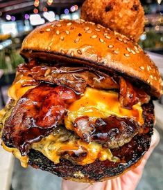 a bacon cheeseburger with onion rings on the side is being held by a person