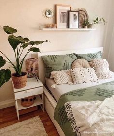 a bed with green and white pillows in a bedroom next to a potted plant