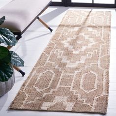 a beige rug with an ornate design on the floor next to a chair and potted plant