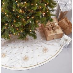 a christmas tree with presents under it on a white tablecloth next to a silver wrapped present box