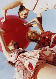 three women are standing in front of a large red ball with their arms around each other