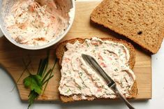 a wooden cutting board topped with sliced bread and a bowl of cream cheese next to it