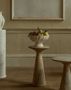 two white vases with fruit in them sitting next to each other on a wooden floor