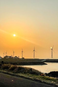 the sun is setting behind windmills in an area with water and grass on both sides