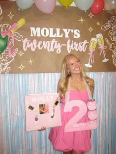 a woman in a pink dress is holding a sign and posing for the camera with balloons around her