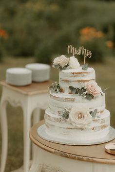 a three tiered cake with flowers on the top is sitting on a small table