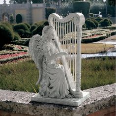 a white statue sitting on top of a stone wall next to a lush green field