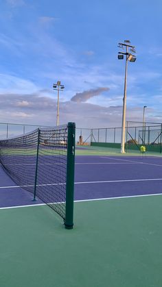 a tennis court with a net and lights on the other side of it, in front of a blue sky