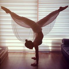 a woman doing a handstand in front of a window with sheer drapes